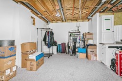 Unfinished basement space featuring exposed wood joists and ductwork, white painted walls, light grey carpeting, and built-in white cabinetry with a countertop - 