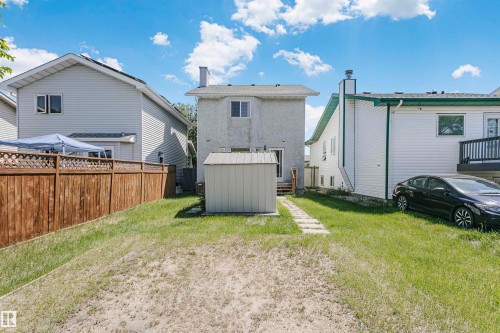 Rear exterior featuring a light-colored siding, a small storage shed, a stone paver pathway, and a wooden fence - 1612 80A Street, Edmonton, AB 