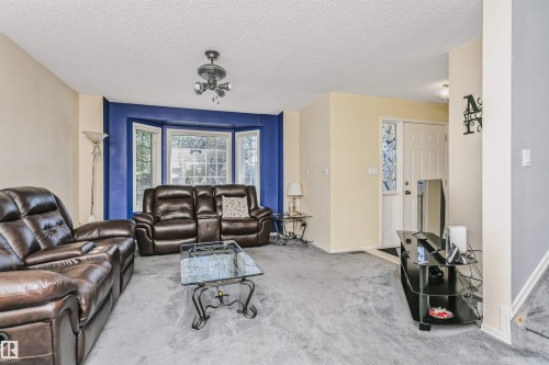 Living area featuring a prominent bay window, neutral wall tones with an accent wall, ceiling fan light fixture, and carpet flooring - 1612 80A Street, Edmonton, AB 