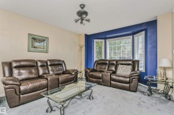 Living area featuring a bay window, ceiling-mounted light fixture, and textured carpeting - 