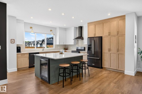Contemporary kitchen featuring a large central island with a built-in beverage cooler, light wood-finish flooring, and a mix of white and natural wood-finish cabinetry - 30 Rosewood Way, St. Albert, AB 