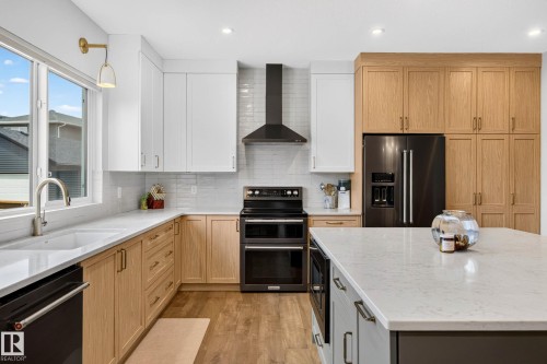 Modern kitchen featuring a two-toned cabinetry scheme, a central island with integrated microwave, a double oven range, and a full suite of black stainless steel appliances - 30 Rosewood Way, St. Albert, AB 