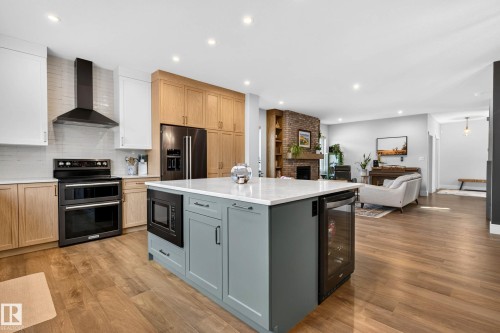 Spacious kitchen featuring a large central island with integrated microwave and beverage cooler, dual-tone cabinetry, professional-grade range with hood, and wood-finish flooring - 30 Rosewood Way, St. Albert, AB 