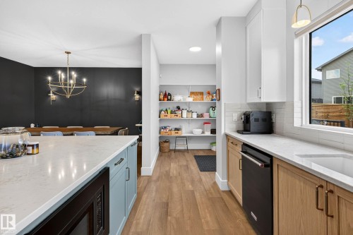Contemporary kitchen featuring a large island with a quartz countertop, wood-finish flooring, and a window with outdoor views - 30 Rosewood Way, St. Albert, AB 