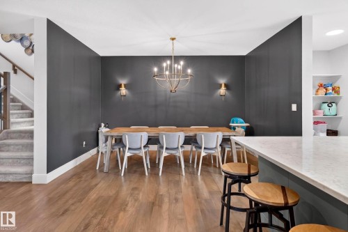 Dining area featuring dark accent walls, wood-finish flooring, a contemporary chandelier, and two wall sconces - 30 Rosewood Way, St. Albert, AB 