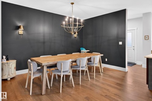 Dining area featuring wood-finish flooring, a contemporary chandelier, two brass wall sconces, and a dark accent wall - 30 Rosewood Way, St. Albert, AB 