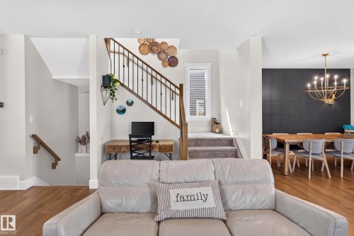 Open-concept living area with wood-finish flooring, a contemporary staircase with dark balusters, a built-in office nook, and a dining area featuring a dark accent wall and a modern chandelier - 30 Rosewood Way, St. Albert, AB 