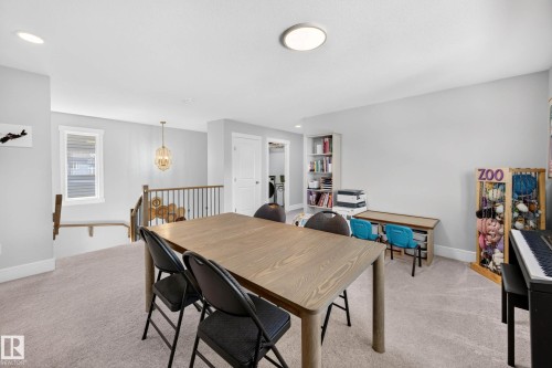 Carpeted upper-level space featuring a contemporary wooden table, a built-in bookshelf, a window, and a chandelier - 30 Rosewood Way, St. Albert, AB 