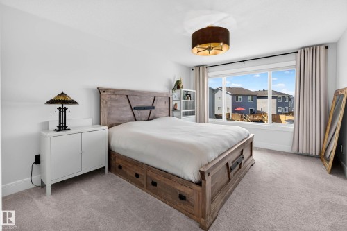 Spacious room featuring light-toned carpet flooring, a large window with white trim, and a contemporary drum pendant light fixture - 30 Rosewood Way, St. Albert, AB 