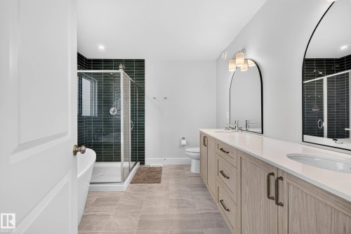Dual vanity with light wood-finish cabinetry, white countertops, and arched mirrors - 30 Rosewood Way, St. Albert, AB 