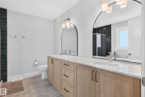 Dual vanity featuring light wood-finish cabinetry, white countertops, and arched mirrors - 30 Rosewood Way, St. Albert, AB 