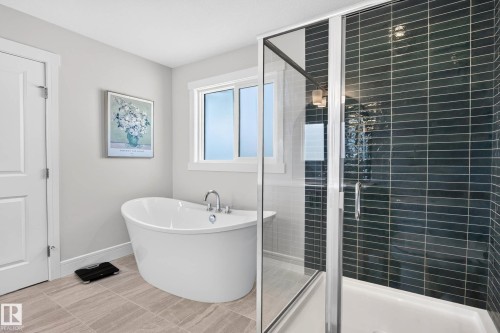 Modern bathroom featuring a glass-enclosed shower with dark tile surround, a freestanding soaking tub with chrome fixtures, and light-toned tile flooring - 30 Rosewood Way, St. Albert, AB 