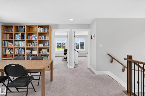 Spacious room with built-in wooden shelving, light gray carpeting, and a wooden handrail with black metal balusters - 30 Rosewood Way, St. Albert, AB 