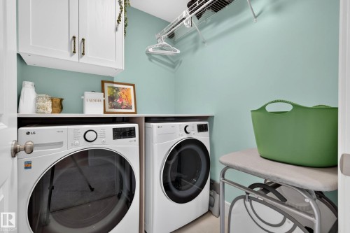 Laundry area featuring front-loading machines, built-in overhead cabinetry with bronze hardware, and a practical storage shelf - 30 Rosewood Way, St. Albert, AB 
