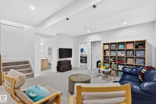 Spacious carpeted recreation room featuring recessed lighting, a built-in shelving unit, and a wall-mounted television - 30 Rosewood Way, St. Albert, AB 