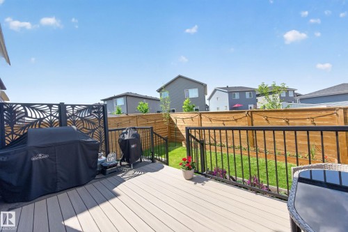 Spacious outdoor deck featuring composite decking, black metal railings, a decorative privacy screen, and a fenced backyard with green lawn - 30 Rosewood Way, St. Albert, AB 