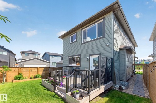 Rear exterior featuring a ground-level deck with black railings, a private side entrance, and a manicured lawn - 30 Rosewood Way, St. Albert, AB 