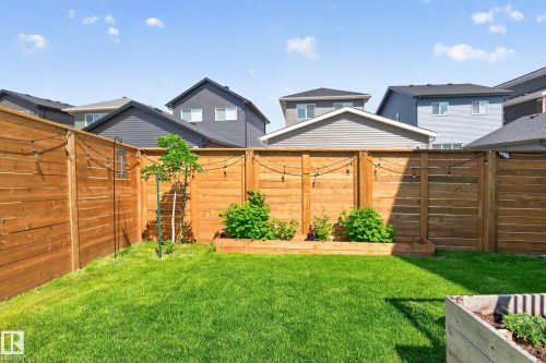Expansive backyard featuring a wood privacy fence, a raised garden bed with plantings, string lighting fixtures, and a small tree - 30 Rosewood Way, St. Albert, AB 