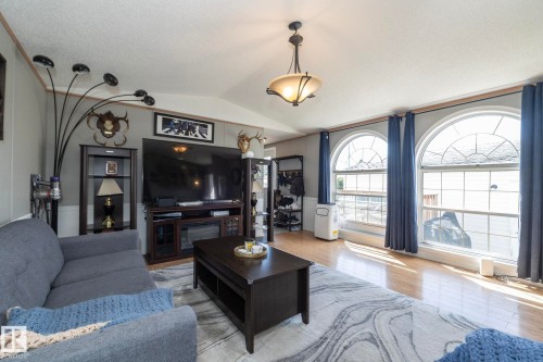 Living area featuring wood-finish flooring, a vaulted ceiling, and two arched windows with grid patterns - 143 48 3400 Street W, Stony Plain, AB 