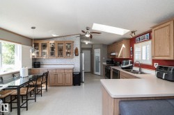 Open concept kitchen and dining area featuring a skylight, light wood cabinetry, white countertops, and stainless steel appliances - 