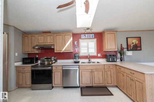 Kitchen featuring a skylight, wood-finish cabinetry, stainless steel appliances, a double basin sink, and a countertop extending into a peninsula - 143 48 3400 Street W, Stony Plain, AB 