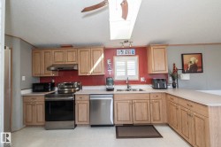 Kitchen featuring a skylight, wood-finish cabinetry, stainless steel appliances, a double basin sink, and a countertop extending into a peninsula - 