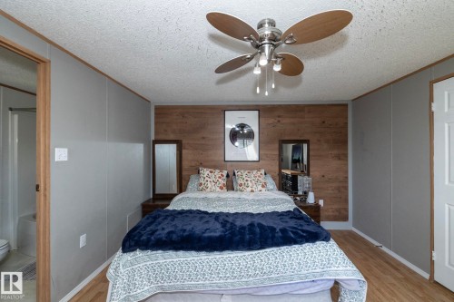 Interior space featuring wood-finish flooring, a textured ceiling, a ceiling fan with integrated lighting, and a prominent wood-panel accent wall - 143 48 3400 Street W, Stony Plain, AB 