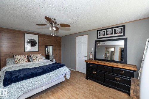 Bedroom featuring a wood-finish accent wall, ceiling fan with integrated lighting, and wood-finish flooring - 143 48 3400 Street W, Stony Plain, AB 