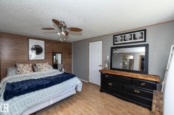Bedroom featuring a wood-finish accent wall, ceiling fan with integrated lighting, and wood-finish flooring - 