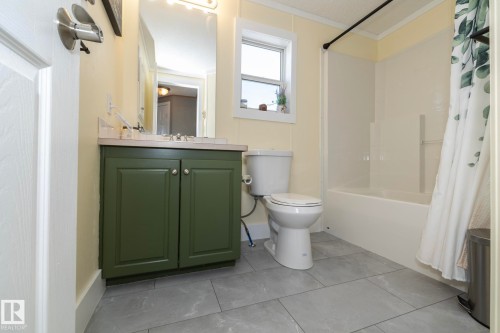 Bathroom featuring a green vanity with a light-colored countertop, a vanity mirror with overhead lighting, a white toilet, and a white bathtub with a shower enclosure - 143 48 3400 Street W, Stony Plain, AB 