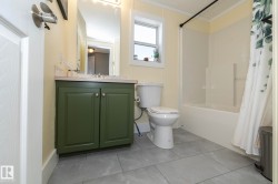 Bathroom featuring a green vanity with a light-colored countertop, a vanity mirror with overhead lighting, a white toilet, and a white bathtub with a shower enclosure - 