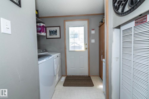 Dedicated laundry area featuring a white washing machine and dryer, a built-in shelving unit, and a rear exterior door with a window - 143 48 3400 Street W, Stony Plain, AB 