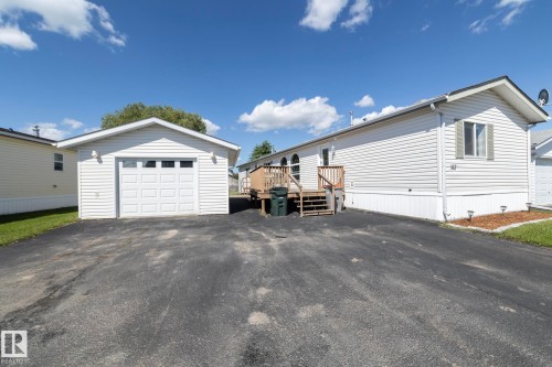 Detached single-car garage featuring a paneled door with upper window inserts, white vinyl siding, and exterior lighting - 143 48 3400 Street W, Stony Plain, AB 