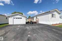 Detached single-car garage featuring a paneled door with upper window inserts, white vinyl siding, and exterior lighting - 