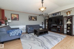 Spacious living area featuring wood-finish flooring, a contemporary ceiling light fixture, and a gray-toned wall with white wainscoting - 
