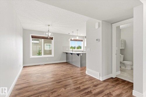 Open-concept living area with wood-finish flooring, a contemporary chandelier, and a bright window - 47 330 Bulyea Road, Edmonton, AB - Indoor