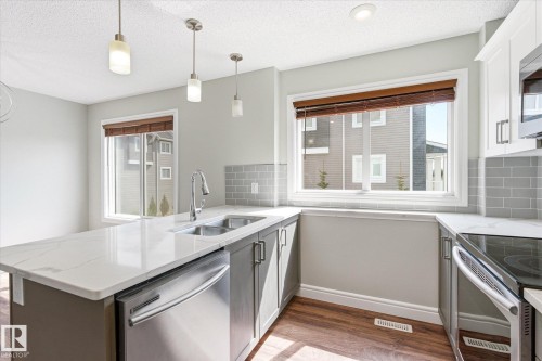Kitchen featuring white quartz countertops, stainless steel appliances, wood-finish flooring, subway tile backsplash, and contemporary pendant lighting - 47 330 Bulyea Road, Edmonton, AB - Indoor Photo Showing Kitchen With Double Sink With Upgraded Kitchen