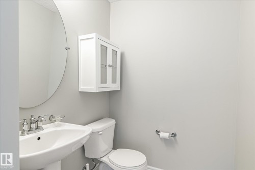 Pedestal sink with chrome faucet, circular wall mirror, and white wall cabinet with glass-paneled doors - 47 330 Bulyea Road, Edmonton, AB - Indoor Photo Showing Bathroom