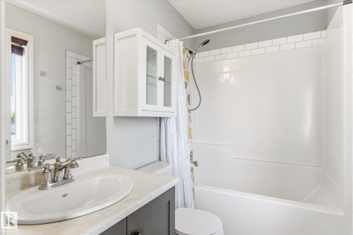 Bathroom featuring a single vanity with a white oval sink and chrome faucet, a wall-mounted medicine cabinet with glass-front doors, a window with a brown roll-down shade, and a bathtub with a white subway tile surround - 47 330 Bulyea Road, Edmonton, AB - Indoor Photo Showing Bathroom