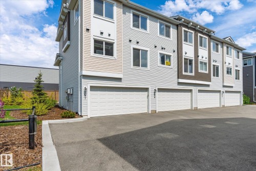 Multi-level townhouse exterior featuring light-colored siding, multiple windows, an attached garage with a white door, and a paved driveway - 47 330 Bulyea Road, Edmonton, AB - Outdoor