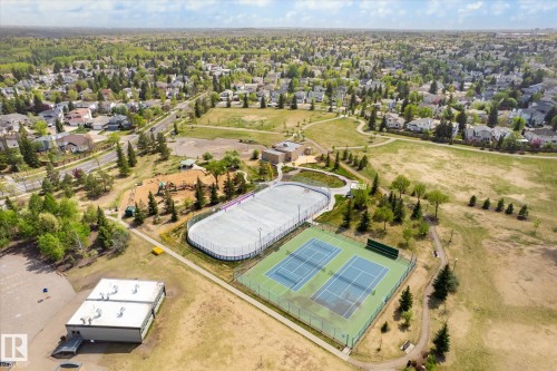 Expansive community greenspace featuring two tennis courts, an ice rink, and a play structure, surrounded by residential properties and mature trees - 47 330 Bulyea Road, Edmonton, AB - Outdoor With View