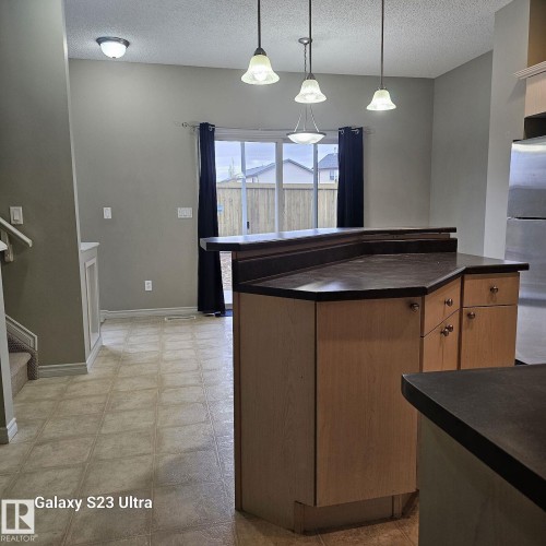 Kitchen island featuring a dark countertop, light wood-finish cabinetry, and pendant lighting - 99 13825 155 Avenue, Edmonton, AB 