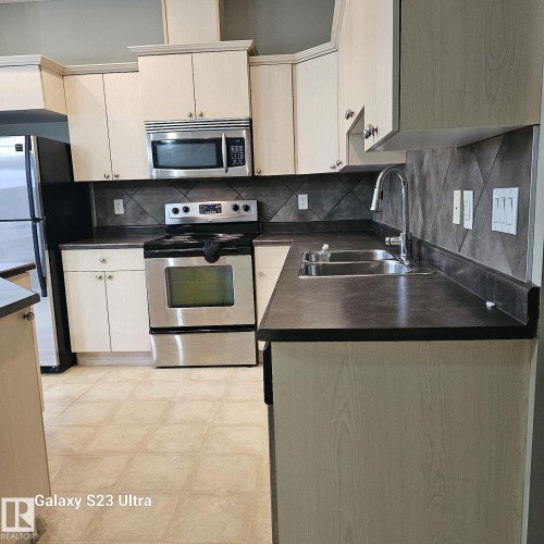 Kitchen featuring light wood-finish cabinetry, dark countertops, and a full suite of stainless steel appliances - 99 13825 155 Avenue, Edmonton, AB 
