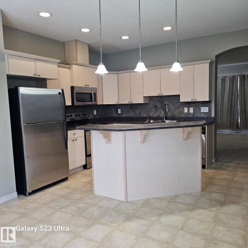 Kitchen featuring light wood-finish cabinetry, stainless steel appliances, a center island with countertop seating, recessed lighting, and pendant fixtures - 99 13825 155 Avenue, Edmonton, AB 