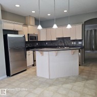 Kitchen featuring light wood-finish cabinetry, stainless steel appliances, a center island with countertop seating, recessed lighting, and pendant fixtures - 