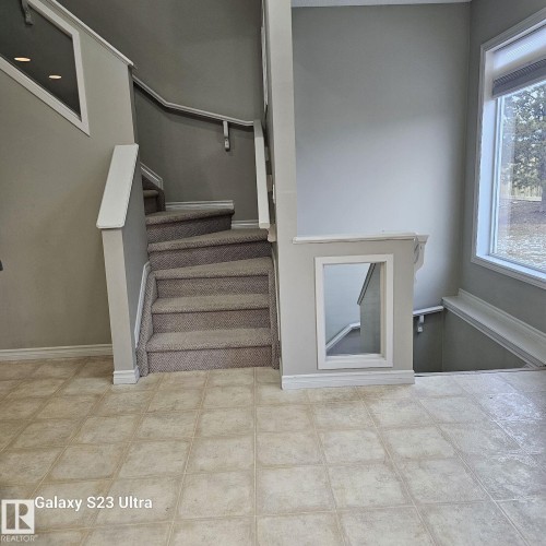 Carpeted staircase with white railings and an integrated wall niche, complemented by neutral wall paint and tile flooring - 99 13825 155 Avenue, Edmonton, AB 
