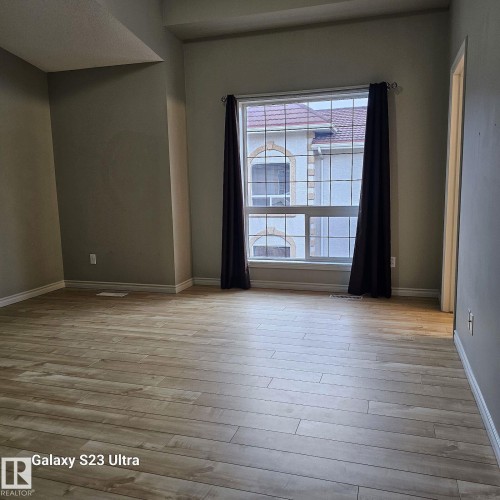 Spacious room featuring light wood-finish flooring, a large multi-pane window, and high ceilings - 99 13825 155 Avenue, Edmonton, AB 