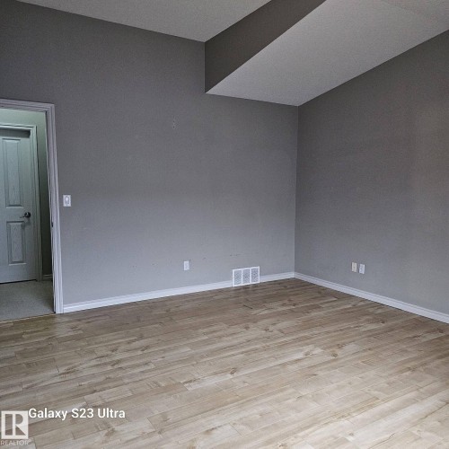 Spacious room featuring light wood-finish flooring, neutral gray wall paint, white trim, and a white interior door - 99 13825 155 Avenue, Edmonton, AB 