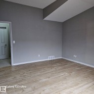 Spacious room featuring light wood-finish flooring, neutral gray wall paint, white trim, and a white interior door - 
