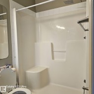 White acrylic shower enclosure featuring a built-in bench and recessed shelving - 